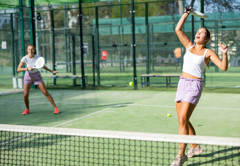Obraz premium Two young active women tennis players with rackets playing padel on an outdoor court