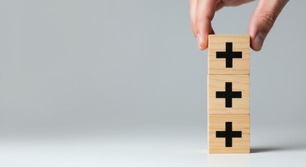 Hand placing the final block on a stack of wooden blocks with plus signs on a plain background