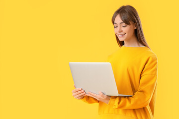 Fototapeta premium Young woman using laptop on yellow background