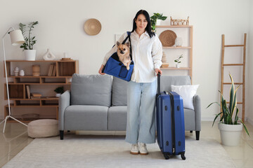 Fototapeta premium Beautiful young woman with suitcase and cute chihuahua dog in pet carrier at home