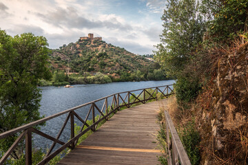 Alamal walkway along the Tagus River with Belver Castle in the background, in Portugal, at sunset.