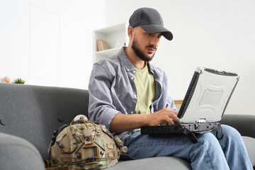 Young soldier working with military laptop on sofa at home
