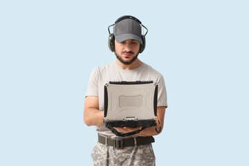 Young soldier working with military laptop on light background