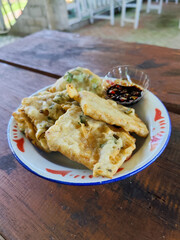 Tempe Mendoan is a traditional Indonesian street snack. Tempe mendoan on a classic iron plate, served with soy sauce, on a wooden table in a stall.