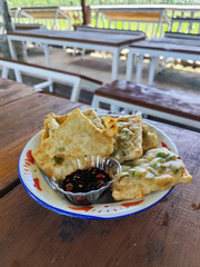 Tempe Mendoan is a traditional Indonesian street snack. Tempe mendoan on a classic iron plate, served with soy sauce, on a wooden table in a stall.