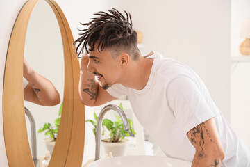 Young man with dreadlocks looking in mirror at home