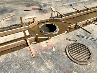 Road repair showing manhole, wooden framing, and open stormwater drain, construction site work in progress urban infrastructure maintenance.