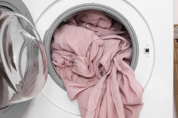 Washing machine with pink bed sheets in laundry room, closeup