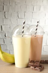 Tasty milkshakes in plastic cups and ingredients on wooden table, closeup