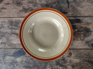 A vintage ceramic plate with brown rim on rustic wooden table background.

