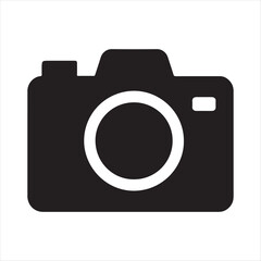 Simple black silhouette of a modern digital camera icon with a white lens ring on a white background