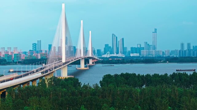 Aerial shot of a modern cable-stayed bridge spanning a wide river with the city skyline in Nanjing, China.