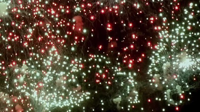 Spectacular fireworks light up the dark sky. Red and white bursts create an awe-inspiring display of celebration during an Independence Day festival in America.