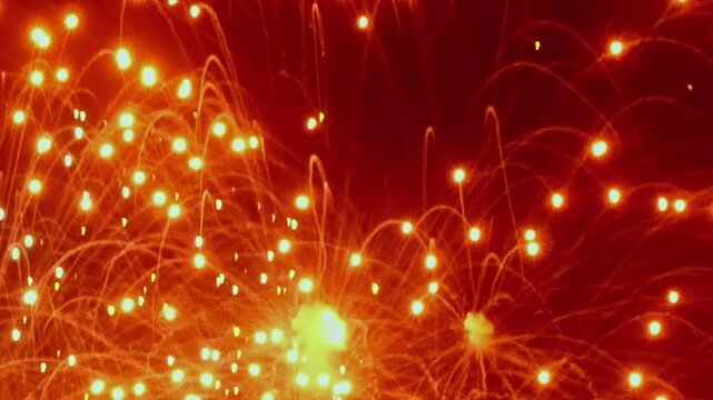 Vibrant bursts of fiery orange and golden light explode in the dark evening sky. Celebration fills the air as dazzling patterns dance and shimmer with festive joy.