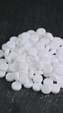 Vertical video sugar substitute tablets rotating on black surface macro. Artificial sweetener pills zero calories