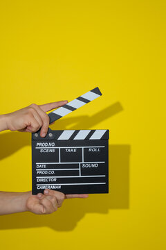 Close up of hands holding a classic movie clapperboard on a yellow background, concept of filming, audiovisual recording, start of shooting, film production, and visual entertainment