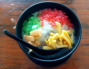 Es Teler, a popular Indonesian dessert served in a black bowl, featuring shaved ice with toppings such as jackfruit, grass jelly, tapioca pearls, and sweet condensed milk