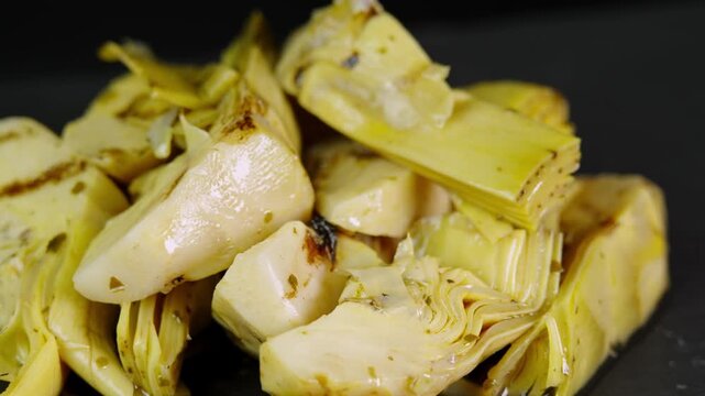 Marinated grilled artichokes rotating on black background. Canned artichokes in oil. Pickled artichoke in marinade