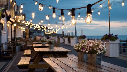 Outdoor cafe seating area with string lights at dusk by the water.