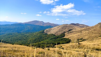 Scenic landscape of the Bieszczady Mountains in Poland, with rolling hills covered by green forests and golden Połonina meadows in autumn.   © VandreVerden