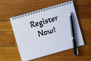 Register now ! written in a notebook on wooden desk