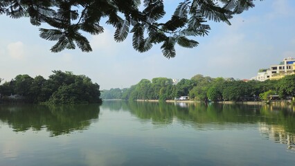 The tranquil Hoan Kiem Lake in Hanoi, Vietnam, is surrounded by lush greenery, offering a peaceful and scenic atmosphere.