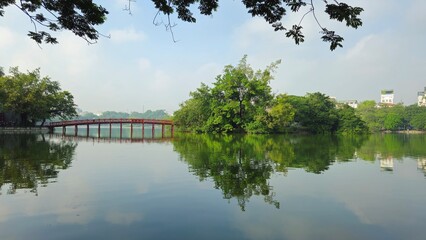 Hoan Kiem Lake in Hanoi, Vietnam, with the iconic red The Huc Bridge reflecting on the calm water.