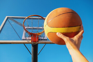 Person holding basketball near hoop. Game outdoor on sunny day. Player about to shoot ball.