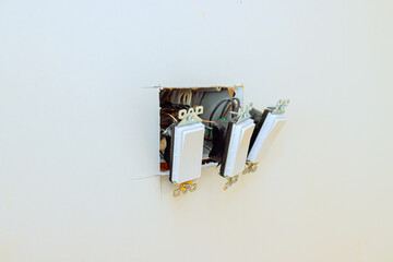 Three electrical switches are installed in newly cut wall opening as part of home renovation work in progress.