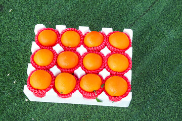 Naklejka premium Fresh Oranges in Red Protective Mesh Packaging on Grass - Premium Citrus Fruit Gift Box Display