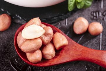 Fresh peanut kernels in wooden spoon on dark slate background