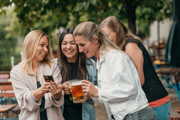 Cheerful women drinking beer with cell phones in a traditional Bavaria beer garden enjoying friendship celebration and leisure time