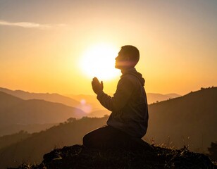 Silhouette of a person praying at sunrise on a mountaintop with mountains visible in the misty background and a sunburst effect