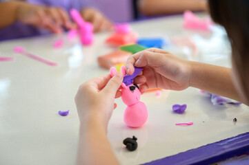 Children making colorful playdough animal figure in classroom, hands shaping creative clay art, preschool education and craft skills, fun learning activity with modeling clay.