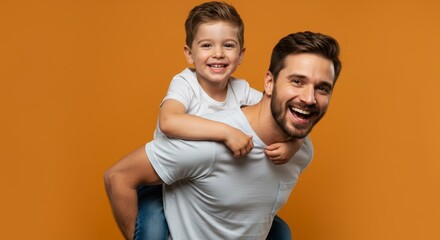 Cheerful father piggybacking his son against a vibrant orange backdrop in studio