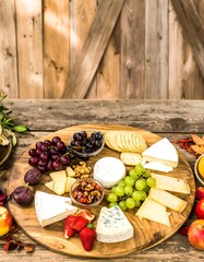 Round wooden cheese board with assorted cheeses, fruits, nuts, and crackers. Autumnal decor
