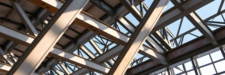 Abstract industrial steel beams create striking patterns in natural construction lighting.