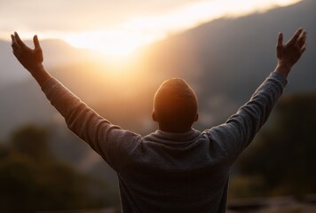 Silhouette of a person facing sunset, arms raised, blurred mountain backdrop evokes peace, serenity, and nature's embrace
