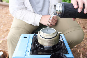 Unrecognizable person pouring water in a kettle to heat it with a travel gas stove, outdoors.