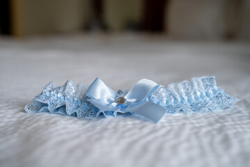 Close up of blue lace bridal garter with satin bow on bed.