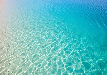 Crystal clear turquoise water gently laps onto a sandy shore, with sunlight creating shimmering patterns on the seabed below