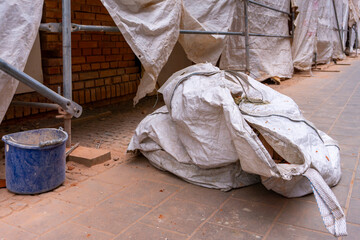 Large construction bag covered with tarp lying on renovation site near scaffolding and brick wall.