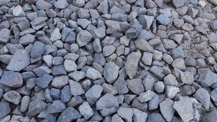 Close-up view of a pile of irregular gray stones and gravel, creating a textured natural background for construction or landscaping use.
