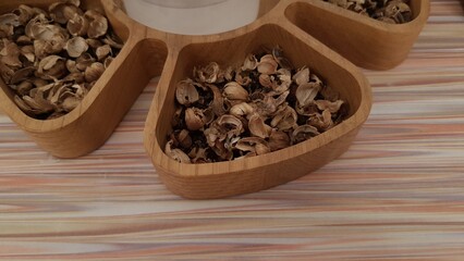 A wooden sectioned tray filled with a variety of dried herbs used for spa treatments. These herbs are commonly used for their aromatic and therapeutic properties in massages, scrubs, and herbal compre
