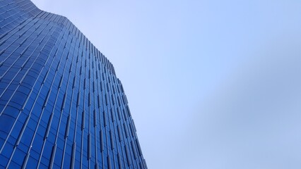 Upward view of a sleek, reflective glass skyscraper with geometric patterns, rising against a bright, open blue sky in an urban setting.  
