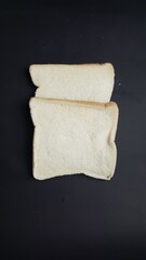 Minimalist top view of two plain white bread slices placed on a dark black surface, highlighting texture and simplicity.  
