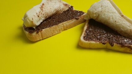 Close-up of sliced bread with rich chocolate spread filling, folded into sandwiches, placed against a bright yellow surface.  
