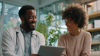 Happy African American Doctor and Patient Laughing While Looking at Tablet - Powered by Adobe