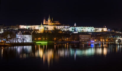 Obraz premium A picturesque evening view of the Prague additions - the Vltava River and the illuminated Prague Castle with the Goitic Cathedral.