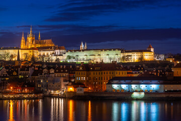 Obraz premium A picturesque evening view of the Prague additions - the Vltava River and the illuminated Prague Castle with the Goitic Cathedral.